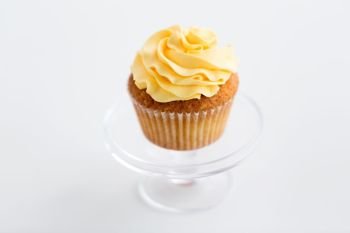 food, pastry and sweets concept - cupcake with yellow buttercream frosting on glass confectionery stand over white background. cupcake with frosting on confectionery stand