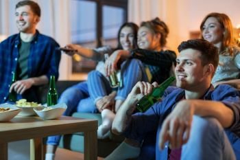friendship and leisure concept - happy friends with non-alcoholic drinks watching tv at home in evening. happy friends with drinks watching tv at home