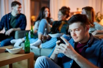 technology, internet addiction and people concept - man with smartphone at home friends party in evening. man with smartphone at home party