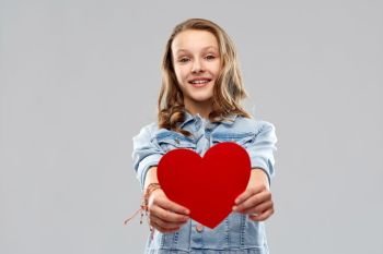 valentine’s day, love and people concept - smiling pretty teenage girl in denim jacket holding red heart over grey background. smiling teenage girl with red heart