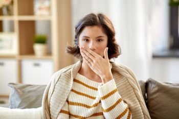 cold and health problem concept - sick woman in blanket coughing or covering mouth by hand at home. sick woman in blanket coughing at home