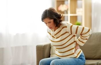 people, healthcare and problem concept - unhappy woman suffering from pain in back or reins at home. unhappy woman suffering from backache at home