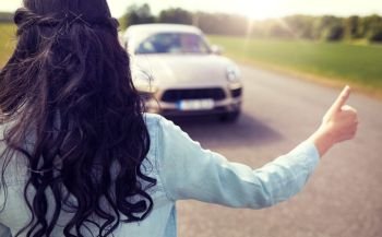 road trip, travel, gesture and people concept - woman hitchhiking and stopping car with thumbs up gesture at countryside . woman hitchhiking and stopping car with thumbs up