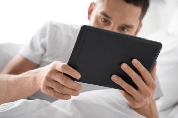 technology, internet and people concept - close up of young man with tablet pc computer in bed at home bedroom in morning. close up of man with tablet computer in bed