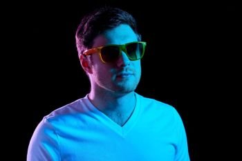 leisure, clubbing and nightlife concept - portrait of young man in sunglasses at dark room over ultra violet neon lights. man in sunglasses over ultra violet neon lights
