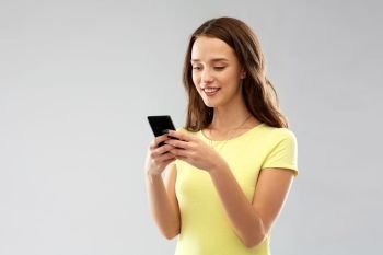 technology and people concept - smiling young woman or teenage girl in blank yellow t-shirt using smartphone over grey background. young woman or teenage girl using smartphone