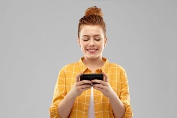 technology, communication and people concept - smiling red haired teenage girl in checkered shirt using smartphone over grey background. smiling red haired teenage girl using smartphone