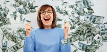 success, jackpot and finances people concept - happy laughing senior woman in glasses celebrating triumph under money falling from above over grey background. happy senior woman celebrating success over money