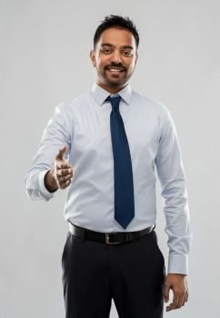 business, office worker and people concept - smiling indian businessman stretching hand out for handshake over grey background. indian businessman stretching hand for handshake