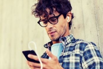 people, music, technology, leisure and lifestyle - happy young hipster man with earphones and smartphone listening to music. man with earphones and smartphone listening music