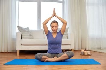 mindfulness, spirituality and healthy lifestyle concept - woman meditating in lotus pose at home. woman meditating in lotus pose at home