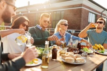 leisure and people concept - happy friends eating and drinking at barbecue party on rooftop. friends having dinner or bbq party on rooftop