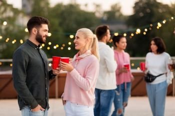 leisure, celebration and people concept - happy friends clinking drinks in party cups toasting at rooftop. friends with drinks in party cups at rooftop