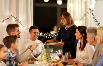 celebration, holidays and people concept - happy senior woman offering roast chicken to family having dinner party at home. happy family having dinner party at home