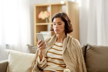 technology and people concept - sad young woman in blanket using smartphone at home. sad woman in blanket using smartphone at home
