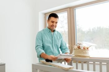 parenthood, fatherhood and nursery concept - happy middle-aged father with user manual assembling baby bed at home. father with manual assembling baby bed at home