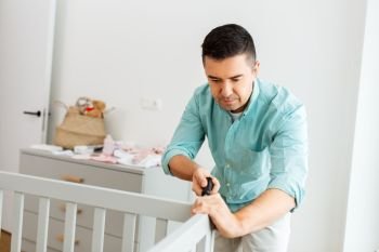 parenthood, fatherhood and nursery concept - happy middle-aged father with screwdriver assembling baby bed at home. happy father with screwdriver assembling baby bed