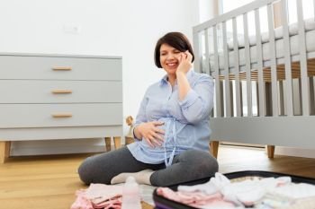 pregnancy, communication and nursery concept - happy pregnant middle-aged woman packing bag or suitcase for maternity hospital and calling on smartphone at home. pregnant woman packing hospital bag and calling