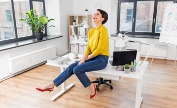 business and people concept - happy laughing businesswoman sitting on desk at office. happy businesswoman sitting on desk at office