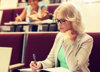 education, high school, university, learning and people concept - student girl writing to notebook in lecture hall. student girl writing to notebook in lecture hall