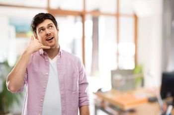 people concept - young man showing phone call gesture over office room background. man showing phone call gesture over office room