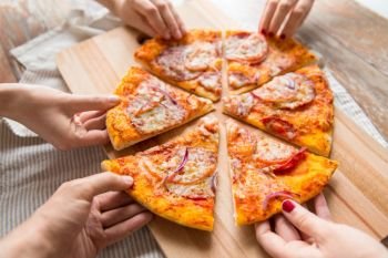 food, people and eating concept - close up of hands sharing sliced homemade pizza on wooden table. close up of hands sharing pizza on wooden table