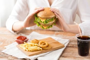 fast food and unhealthy eating concept - close up of woman with double hamburger or cheeseburger, deep-fried squid rings, french fries and cola drink at quick service restaurant. close up of woman eating hamburger at restaurant