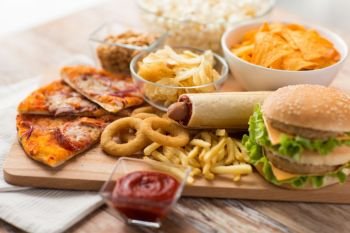 fast food and unhealthy eating concept - close up of double hamburger or cheeseburger, deep-fried squid rings, french fries, pizza and chrisps on wooden board. close up of fast food on wooden board