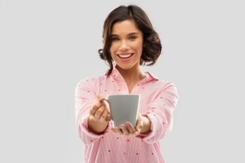 people and bedtime concept - happy young woman in pajama with mug of coffee over grey background. happy young woman in pajama with mug of coffee