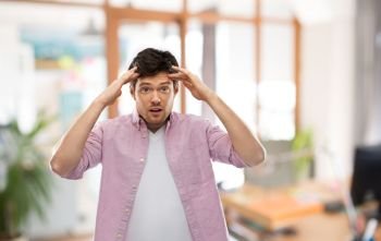 people, concentration and mind concept - man touching his head over office room background. man touching his head over office room