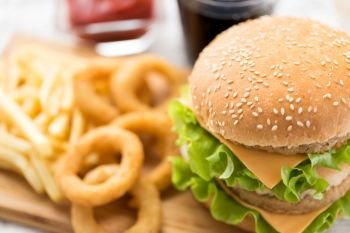 fast food and unhealthy eating concept - close up of double hamburger or cheeseburger, deep-fried squid rings and french fries. close up of hamburger and other fast food