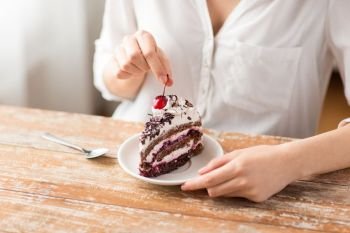 food, unhealthy eating and pastry concept - close up of woman taking cherry from piece of chocolate layer cake. woman taking cherry from piece of chocolate cake