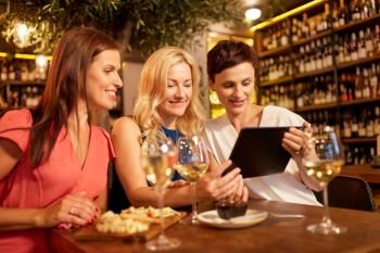 leisure, technology and lifestyle concept - happy women with tablet pc computer at wine bar or restaurant. women with tablet pc at wine bar or restaurant