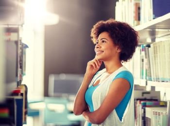 education, high school, university, learning and people concept - happy smiling african american student girl looking for or choosing book at library. african student girl looking for book at library