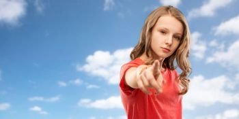 accusing gesture and people concept - teenage girl with long hair in red t-shirt pointing finger to you over blue sky and clouds background. teenage girl in red t-shirt pointing finger to you