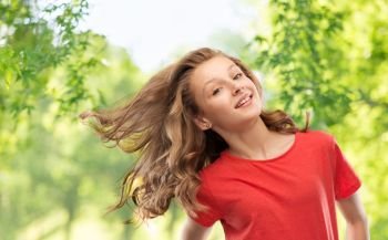 people concept - smiling teenage girl in red t-shirt with long hair waving over green natural background. smiling teenage girl over natural background