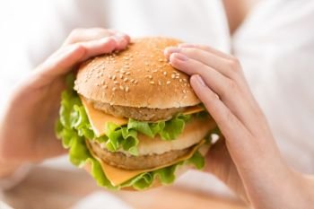 fast food and unhealthy eating concept - close up of woman holding hamburger. close up of woman holding hamburger