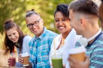 people, friendship and international concept - group of happy friends drinking takeaway coffee and juice talking in park. friends drinking coffee and juice talking in park