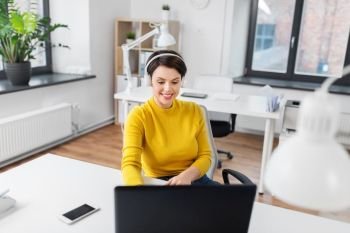business, technology and music concept - smiling businesswoman with headphones, smartphone and laptop computer working at office. businesswoman with headphones and laptop at office