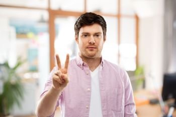 gesture, count and people concept - young man showing two fingers or peace hand sign over office room background. young man showing two fingers over office