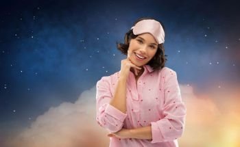 people and bedtime concept - happy young woman in pajama and eye sleeping mask over starry night sky background. happy young woman in pajama and eye sleeping mask
