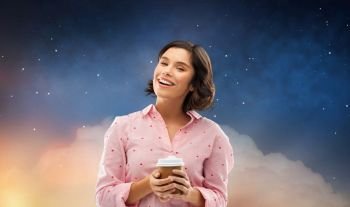 people and bedtime concept - happy young woman in pajama with takeaway paper cup of coffee over starry night sky background. happy young woman in pajama with cup of coffee