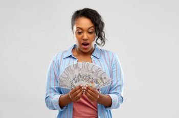 people, finances and winning concept - surprised african american young woman holding fan of dollar money over grey background. surprised african american woman with dollar money