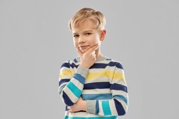 childhood, expressions and people concept - portrait of smiling little boy in striped pullover thinking over grey background. portrait of thinking boy in striped pullover