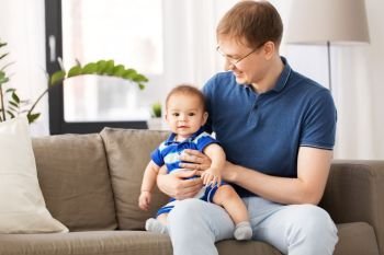 mixed-race family, fatherhood and childhood concept - happy father with baby son sitting on sofa at home. happy father with baby son sitting on sofa at home