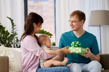 mixed-race family, parenthood and fathers day concept - happy mother with baby boy giving birthday present to father at home. mother with baby giving birthday present to father