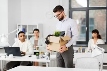 business, firing and job loss concept - fired male office worker with box of his personal stuff and his sad colleagues. sad fired male office worker with personal stuff