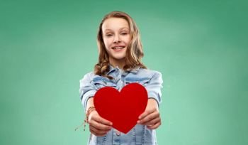 valentine’s day, love and people concept - smiling pretty teenage girl in denim jacket holding red heart over green school chalk board background. girl with red heart over green school chalk board