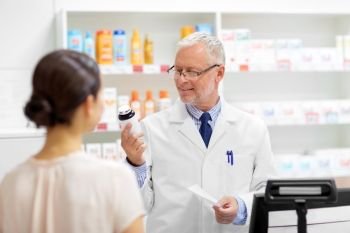 medicine, pharmaceutics, healthcare and people concept - senior apothecary with drug and prescription and female customer at pharmacy. apothecary with cure and customer at pharmacy