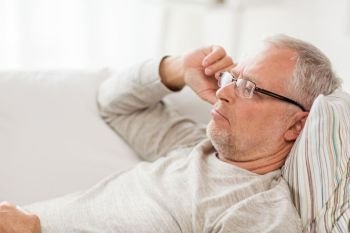 old age, problem and people concept - close up of senior man  lying on sofa and thinking at home. close up of senior man in glasses thinking at home
